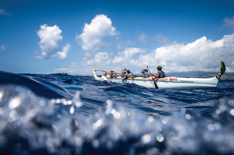 Paddlers in outrigger canoe with ocean waves